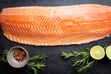 Fresh raw salmon or trout sea fish fillet with spices and herbs on black background, top view