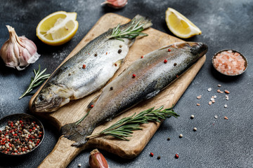 Fresh river trout with spices and ingredient for cooking on dark stone background