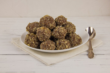Energy balls homemade healthy candies without sugar in a white plate and a spoon on a cotton napkin on a white wooden background