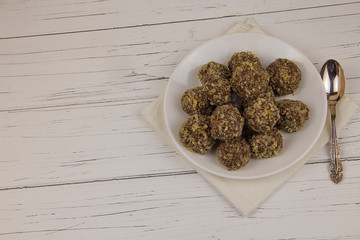 Energy balls homemade healthy candies without sugar in a white plate and a spoon on a cotton napkin on a white wooden background