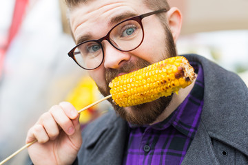 Handsome man eating a delicious corn cob on the street