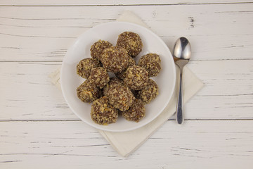 Energy balls homemade healthy candies without sugar in a white plate and a spoon on a cotton napkin on a white wooden background