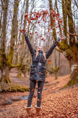 Fototapeta premium Blonde girl throwing leaves in a beautiful forest in winter
