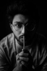 Monochrome fashion portrait of young Indian Bengali brunette man with traditional cotton wear and glasses holding pencil in black copy space background. Indian lifestyle and fashion photograph