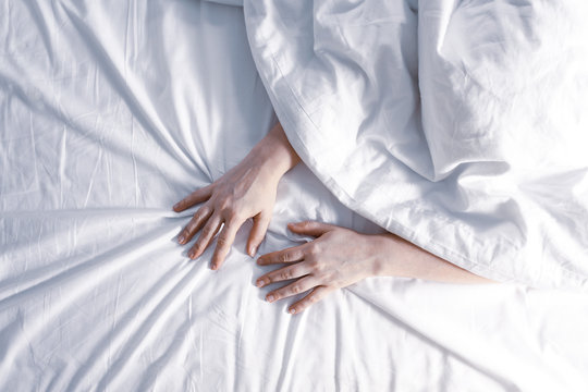 Woman's hands are visible from under the covers as a symbol of fight against insomnia. Tired and exhausted person has nightmares. Toned photo. Top view.