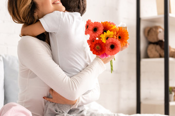 cropped view of happy mother hugging son while holding flowers on mothers day
