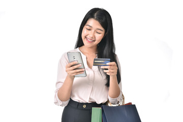 Beautiful Asian woman wearing braces are holding up a credit card and shopping bag happily and she is ordering something by her mobile. Online shopping concept.