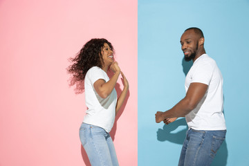 Crazy happy dancing. Young emotional man and woman in casual clothes on pink, blue bicolored background. Concept of human emotions, facial expession, relations, ad. Beautiful african-american couple.