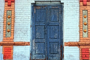 old gray blue closed door on a colored brick wall of a rural building in the street
