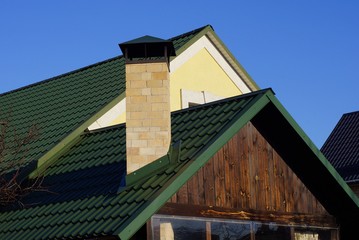 rural house with a brown wooden attic with a green tiled roof and a brick chimney against a blue sky