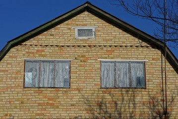 two large windows on an old brown brick attic of a rural house against a blue sky