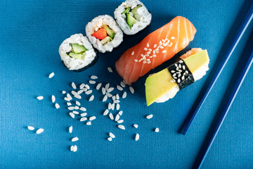Set of sushi and rolls with salmon, avocado and cucumber on a blue background with chopsticks, top view