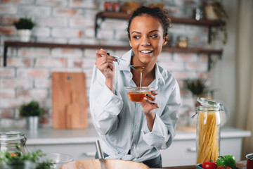 Young woman eating honey. Beautiful mixed race woman in kitchen..