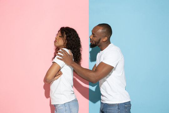 Man apologizing. Young emotional man and woman in casual clothes on pink and blue bicolored background. Concept of human emotions, facial expession, relations, ad. Beautiful african-american couple.