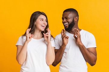 Cheerful interracial couple making wish, pleading for something with crossed fingers