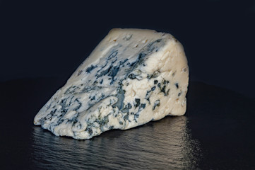 a piece of cheese with blue mould on a black background closeup