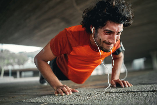 Young Sportsman With Earphones With Painful Face Expression Squeezed Last Push Up - Highly Motivated And Determined Athlete 