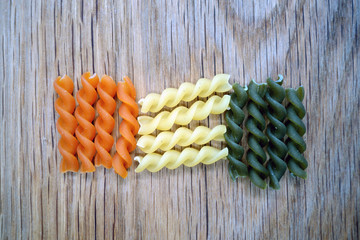 Dry multi-colored pasta on wooden board.