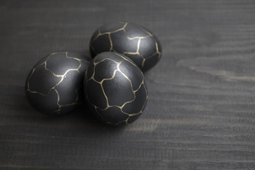 Fototapeta premium Painted eggs in black color with golden patterns on a wooden background. Preparing for the Easter holiday.