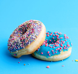 two round baked donut with colored sugar sprinkles and with blue sugar icing