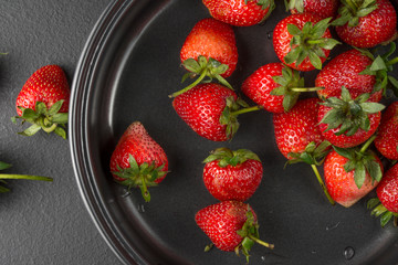 The top view of the red strawberry in the bowl and placed on a black table with a copyspace