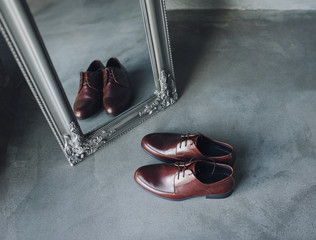 A pair of new brown men's shoes is standing on the gray floor near the mirror. Shoe reflection....