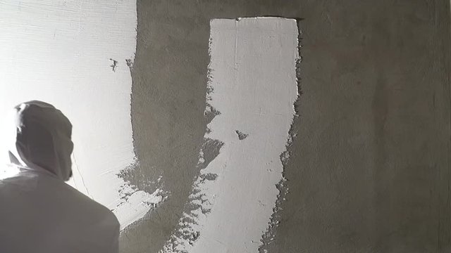 Construction worker plastering and smoothing concrete wall with putty. Putty and leveling walls for subsequent painting. Worker making repair in room. Builder using plastering tool for finishing wall