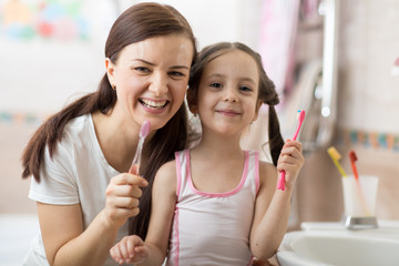 Smiling child girl with her mom brushing and clean teeth in bathroom