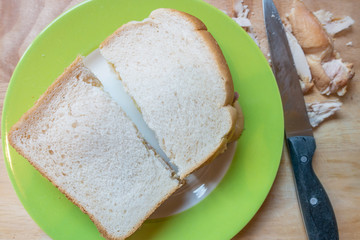 Homemade chicken sandwich with white bread on a green plate on a wooden chopping board for lunch