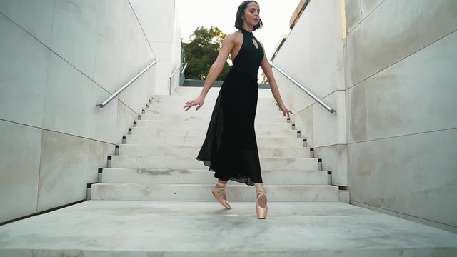 young professional ballerina in black dress is dancing outdoors. ballet dancer is spinning and jumping high in a tutu and pointe shoes. . slow motion