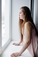 Fototapeta na wymiar Young woman with long hair standing near window and looking out