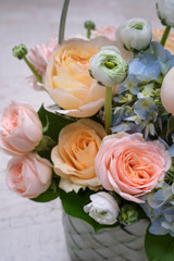 A bouquet of fresh flowers of roses, anemones and gartensium in a basket on a stone background.