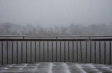 Pier with steel fence with nature background. Snowy weather with lake background.