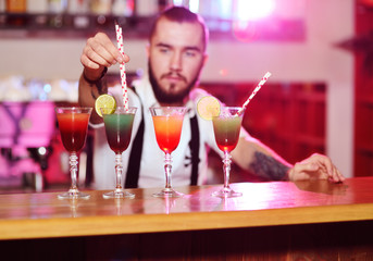 the bartender puts the tubes for cocktails in the prepared alcoholic drinks and smiles against the night club