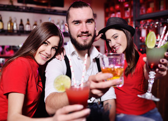 group of friends-young guy and two cute girls having fun at a party holding cocktails