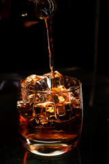 strong alcohol whiskey is poured into a glass with ice closeup