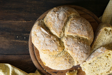Freshly baked homemade bread with seeds, round form and a few pieces. Organic, healthy product on plate, wooden rustic background. Top view, flat lay, copy space. Natural day light. Country food.