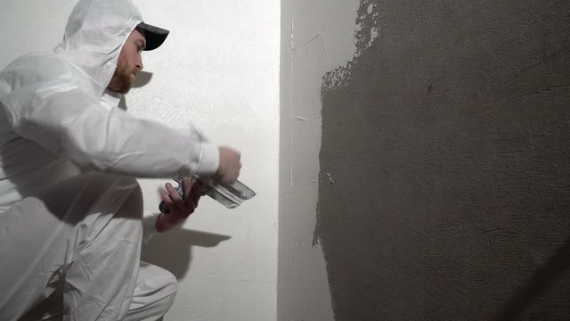 Construction worker plastering and smoothing concrete wall with putty. Putty and leveling walls for subsequent painting. Worker making repair in room. Builder using plastering tool for finishing wall