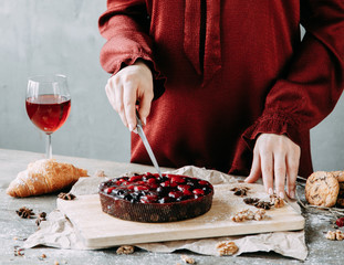Hands of a cook girl with a knife. Berry cake on a wooden Board. Cutting raspberry and cherry pie.