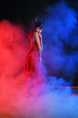 Obraz premium beautiful girl in a black helmet with horns on a blue-red background in smoke