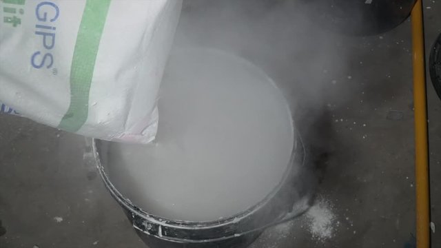 Bucket with white plaster on the construction site. Builder mixing plaster solution in a bucket, using an electric drill. Mortar ingredients mixed in bucket for construction. Plaster concrete	