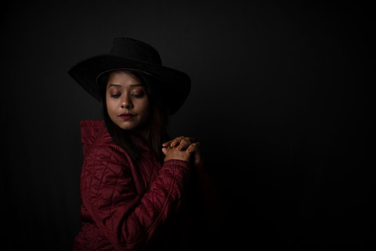 Fashion portrait of an young Indian Bengali brunette woman with maroon winter jacket and cowboy hat in black copy space background. Indian lifestyle and fashion photography.