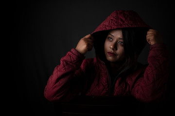 Fashion portrait of an young Indian Bengali brunette woman with maroon winter hoodie jacket in black copy space background. Indian lifestyle and fashion photography.