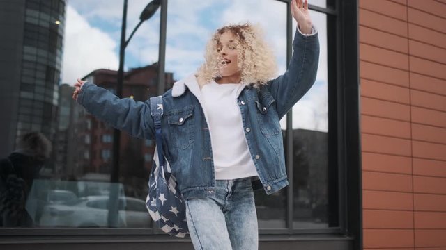 cheerful and carefree girl dancing on the street. Young curly woman having fun and smiling