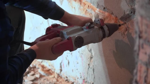 Builder with hammer drill perforator making hole in red brick wall. Man drills a wall with a drill. Drilling a hole in a concrete wall for an electrical outlet