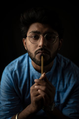 Portrait of young and handsome Indian Bengali brunette man with traditional wear and glasses holding pencil in front of his lips gesturing silence in black copy space background. Indian lifestyle