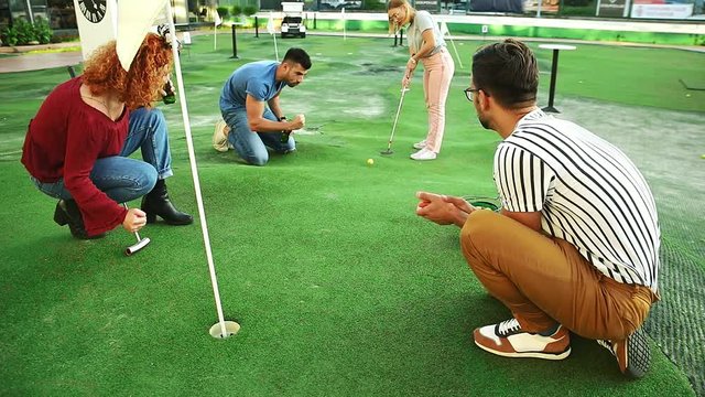 Group of smiling friends enjoying together playing mini golf in the city.
