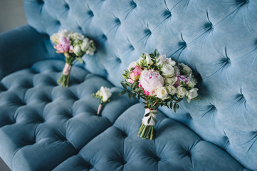 Two multi-colored wedding bouquets with peonies and roses lies on the background of a blue sofa....