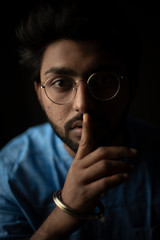 Fashion portrait of young and handsome Indian Bengali brunette man with traditional cotton wear and glasses holding pencil in black copy space background. Indian lifestyle and fashion photograph