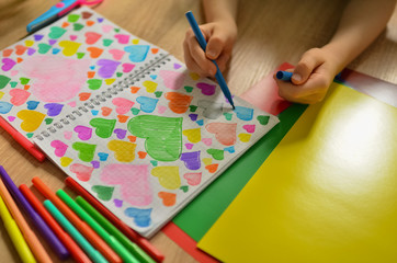  Child's hands draw hearts of different colors in a notebook. Close-up photo.